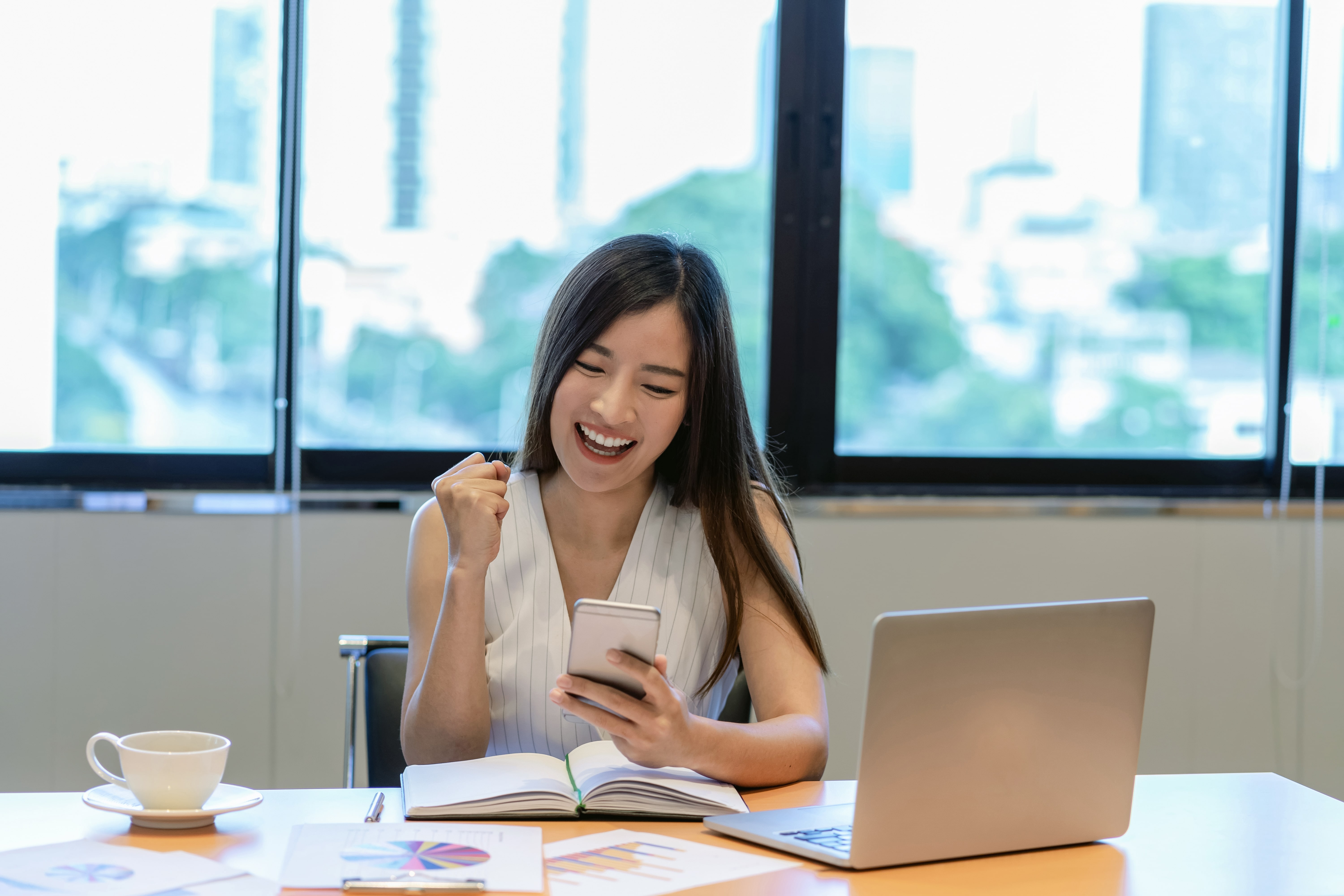 Woman at desk smiling and looking at her phone. She is happy to know that now is a good time to invest in the stock market.